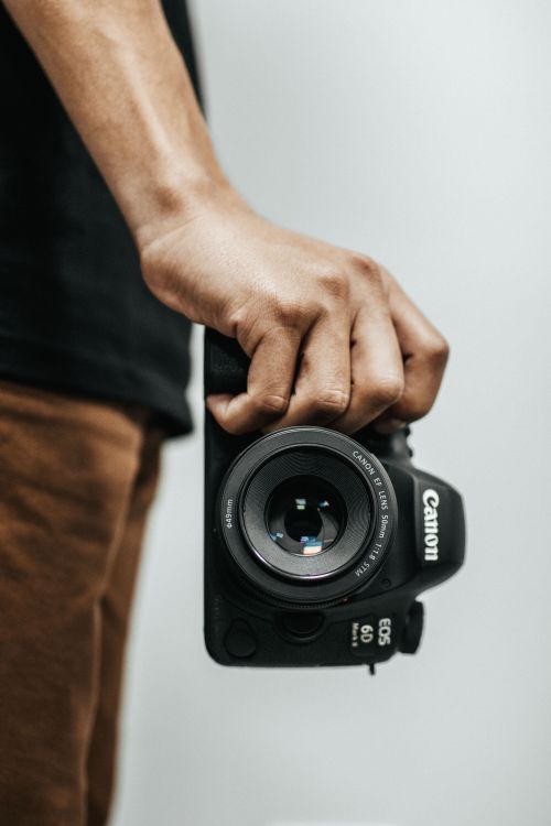 Free A close-up shot of a hand holding a DSLR camera, ideal for photography concepts. Stock Photo