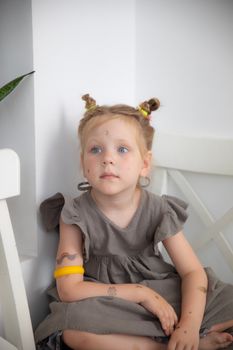 Cute blonde girl with tattoos and gray dress sitting indoors, displaying innocence and fashion photography.