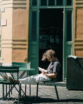 A man reads a book outdoors at a sunlit cafe in Gent, Belgium.