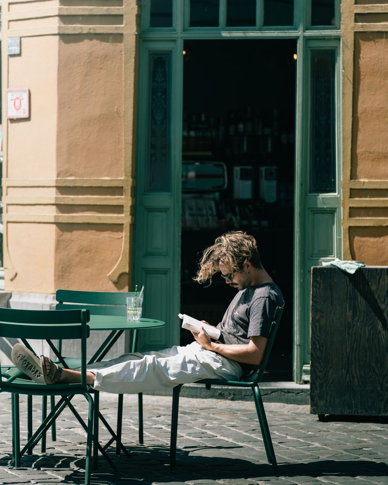 A man reads a book outdoors at a sunlit cafe in Gent, Belgium.
