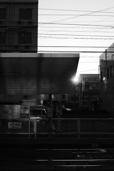 A grayscale urban scene capturing a train station at sunrise with architectural features.