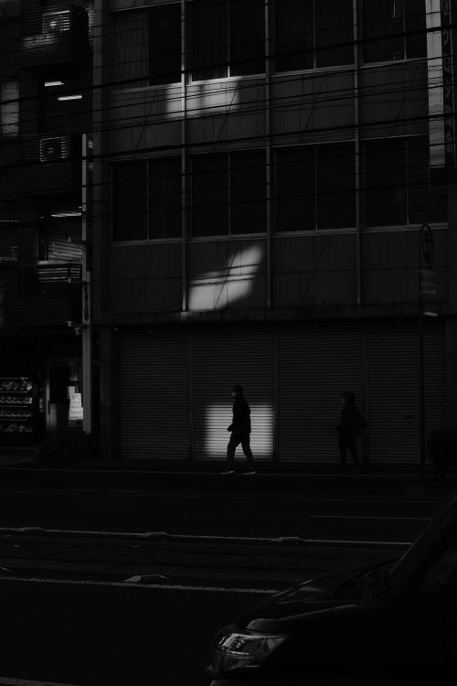 Free A dark and atmospheric street scene capturing silhouettes walking past a shuttered warehouse at night. Stock Photo