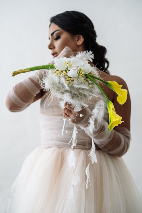 Young Woman Wearing a Wedding Dress Posing against a White Background with a Floral Decoration in Hands