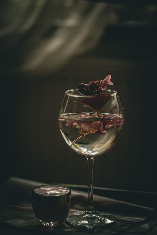 Free A sophisticated wine glass adorned with flowers, creating a romantic ambiance on a dimly lit table. Stock Photo