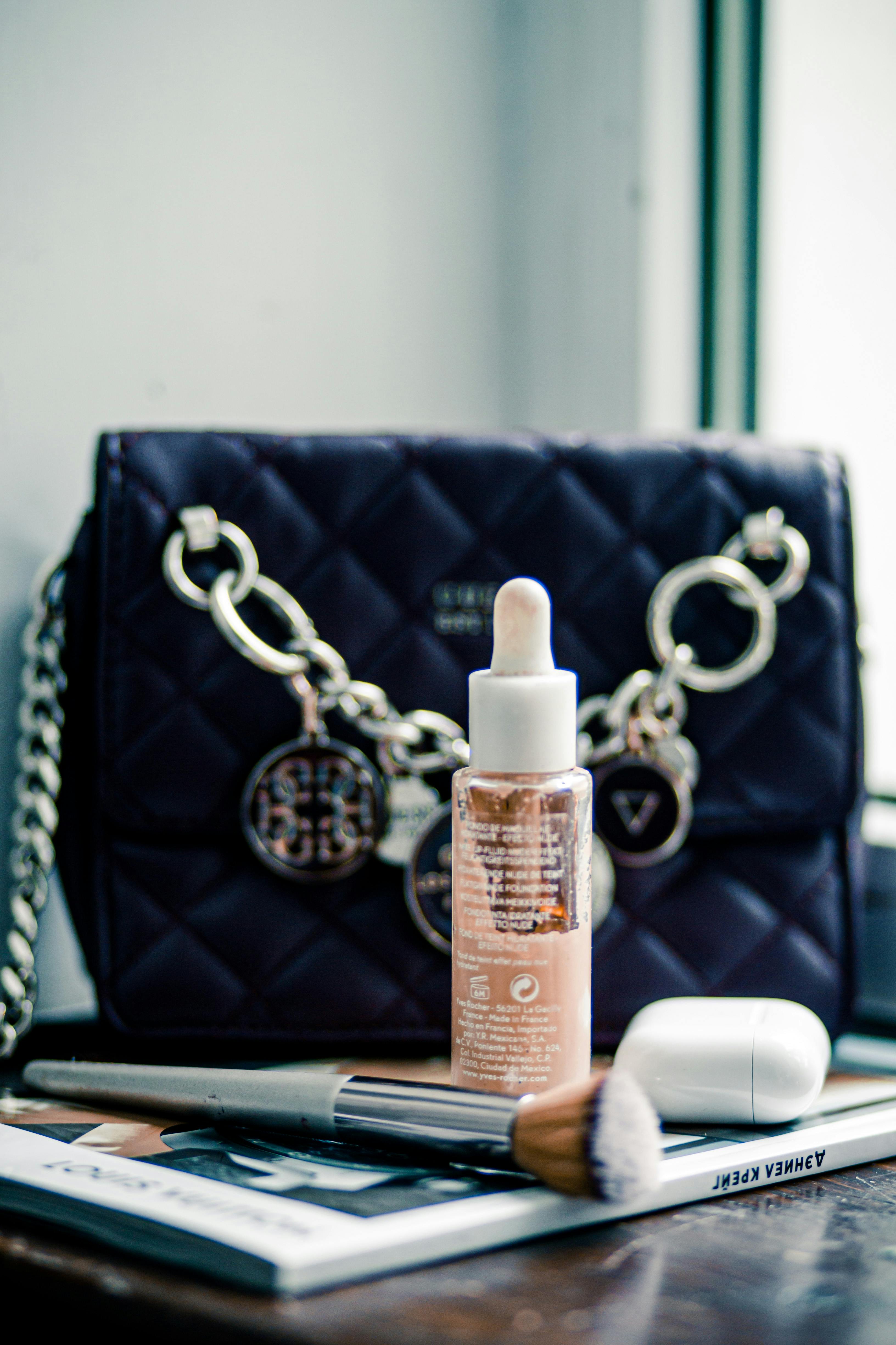 An elegant arrangement of a makeup brush, glass flask and designer bag