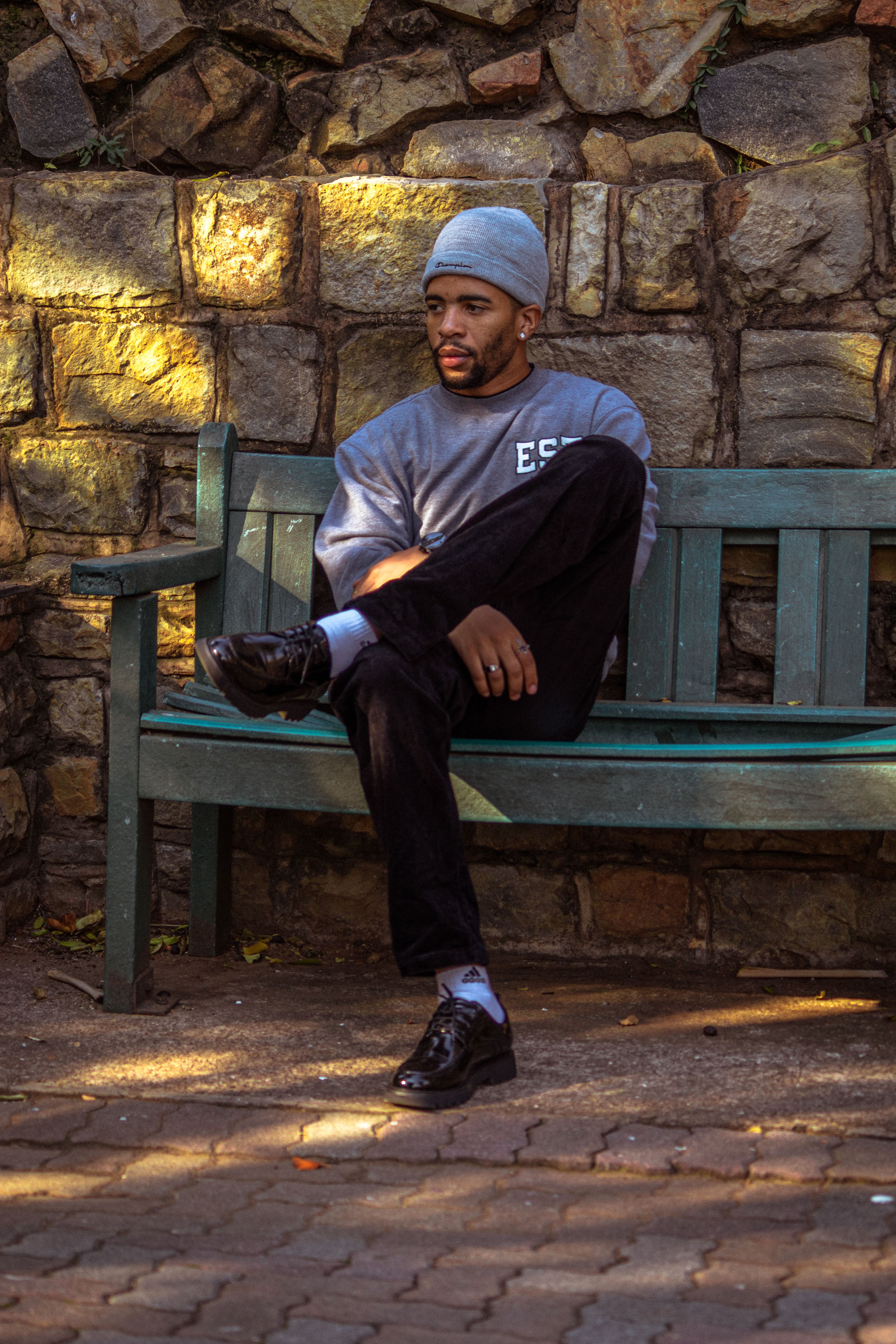 Man in casual attire sitting on a bench against a stone wall outdoors.