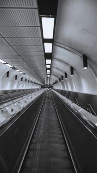 Monochrome view of a long moving walkway in a modern subway station.