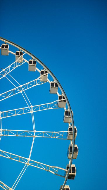 A close-up of a ferris wheel with a clear blue sky background, showcasing metal structure and cabins.