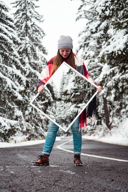A woman carrying a mirror captures snow-covered trees on a winter road.