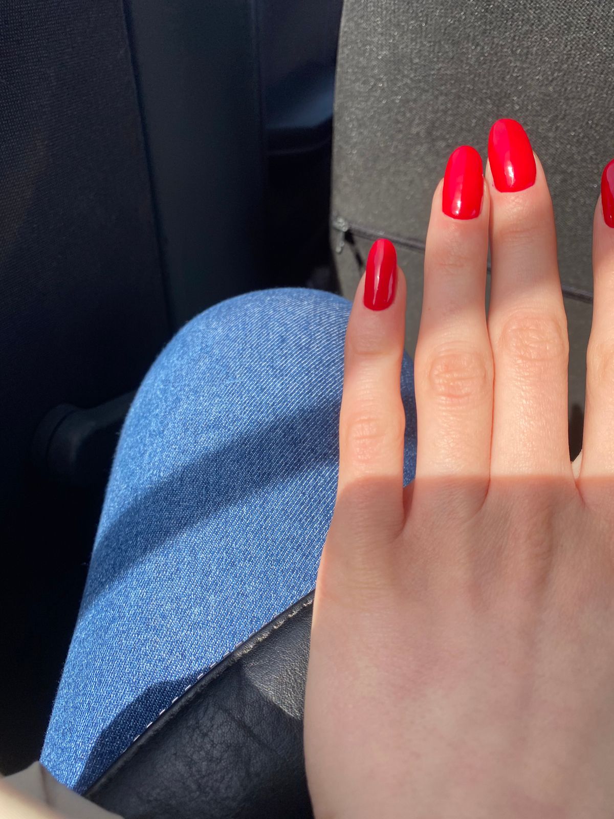 A woman's hand with vibrant red nail polish resting on blue denim in sunlight.
