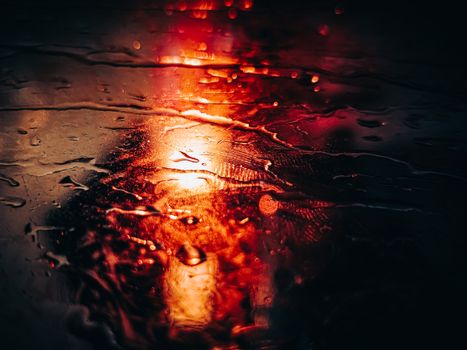 A mesmerizing close-up of raindrops illuminated by a red light on a wet surface at night.