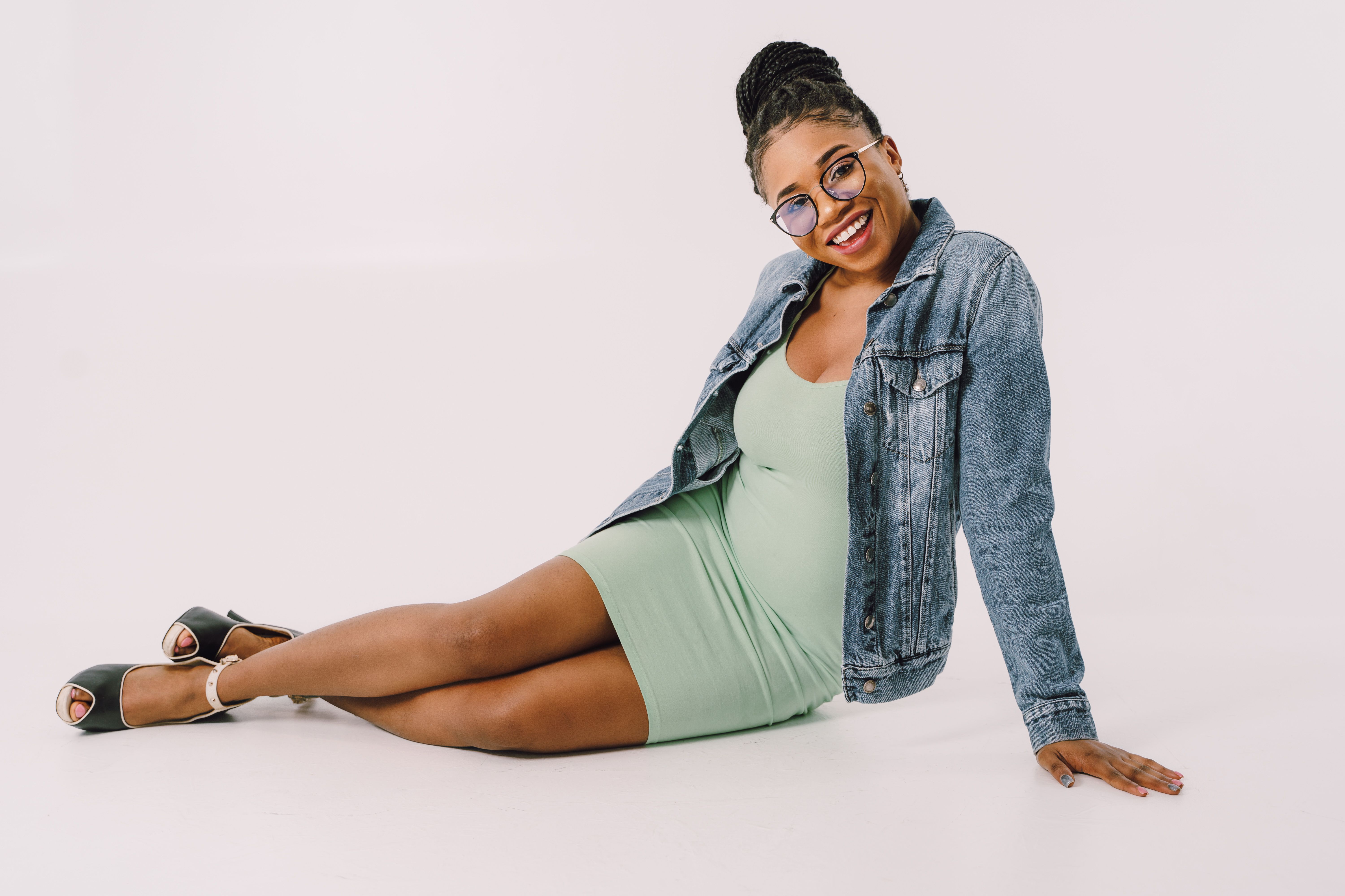 Fashion-forward woman in denim jacket smiling confidently against a white backdrop.