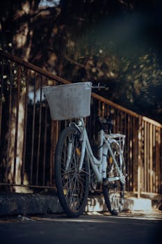 A vintage-style bicycle with a basket leaning against rusty railings in an urban outdoor setting.