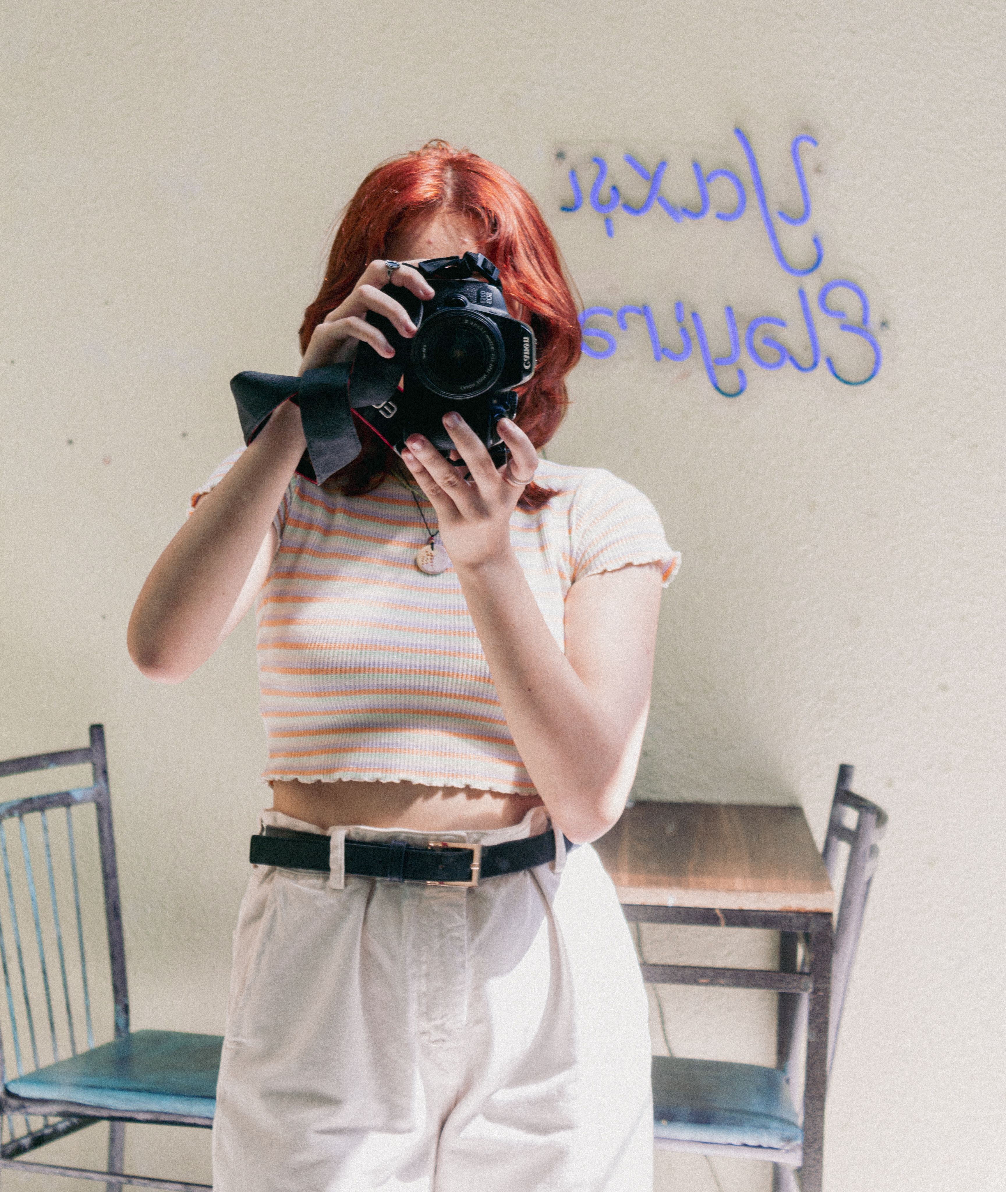 Stylish young woman with red hair taking a photo in a mirror.