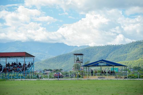 Free People watching a football match in a picturesque countryside stadium with mountain views. Stock Photo