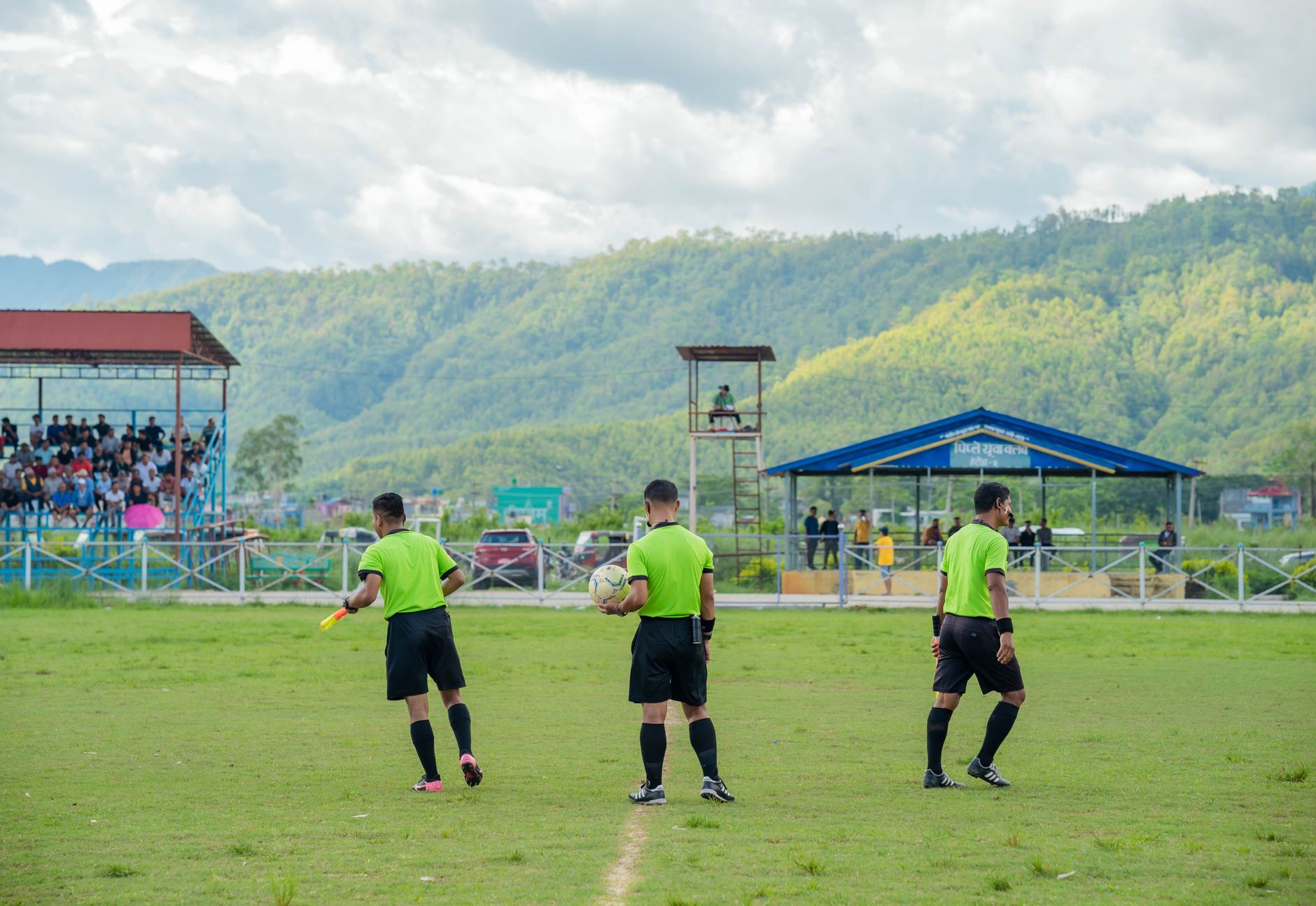 Three referees in green uniforms on a football field during a match.
