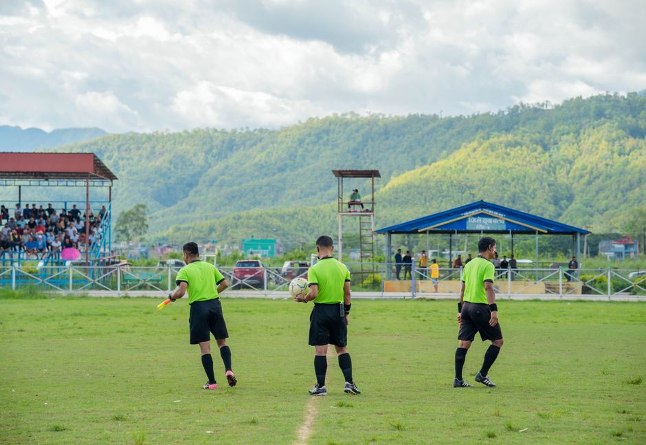 Three referees in green uniforms on a football field during a match.