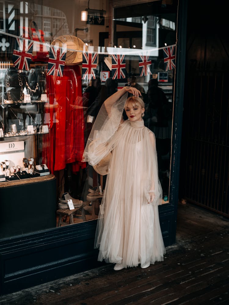 Young Woman In A White Dress Posing Next To Shop Window Display 