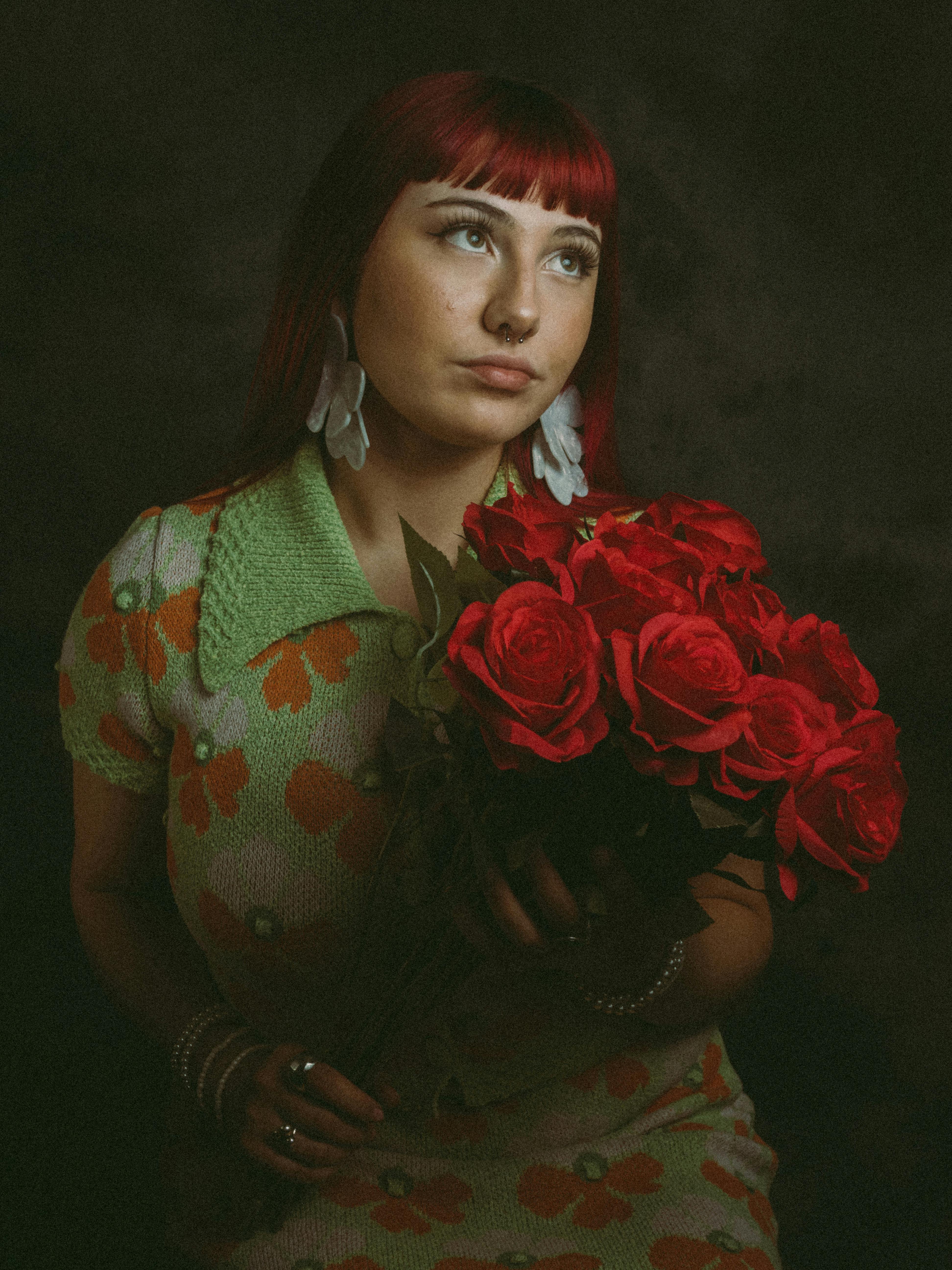Stylish red-haired woman poses with red roses, expressing elegance and modern fashion.