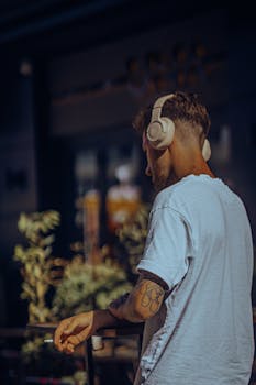Man in white t-shirt with headphones and tattoos, enjoying music outdoors.