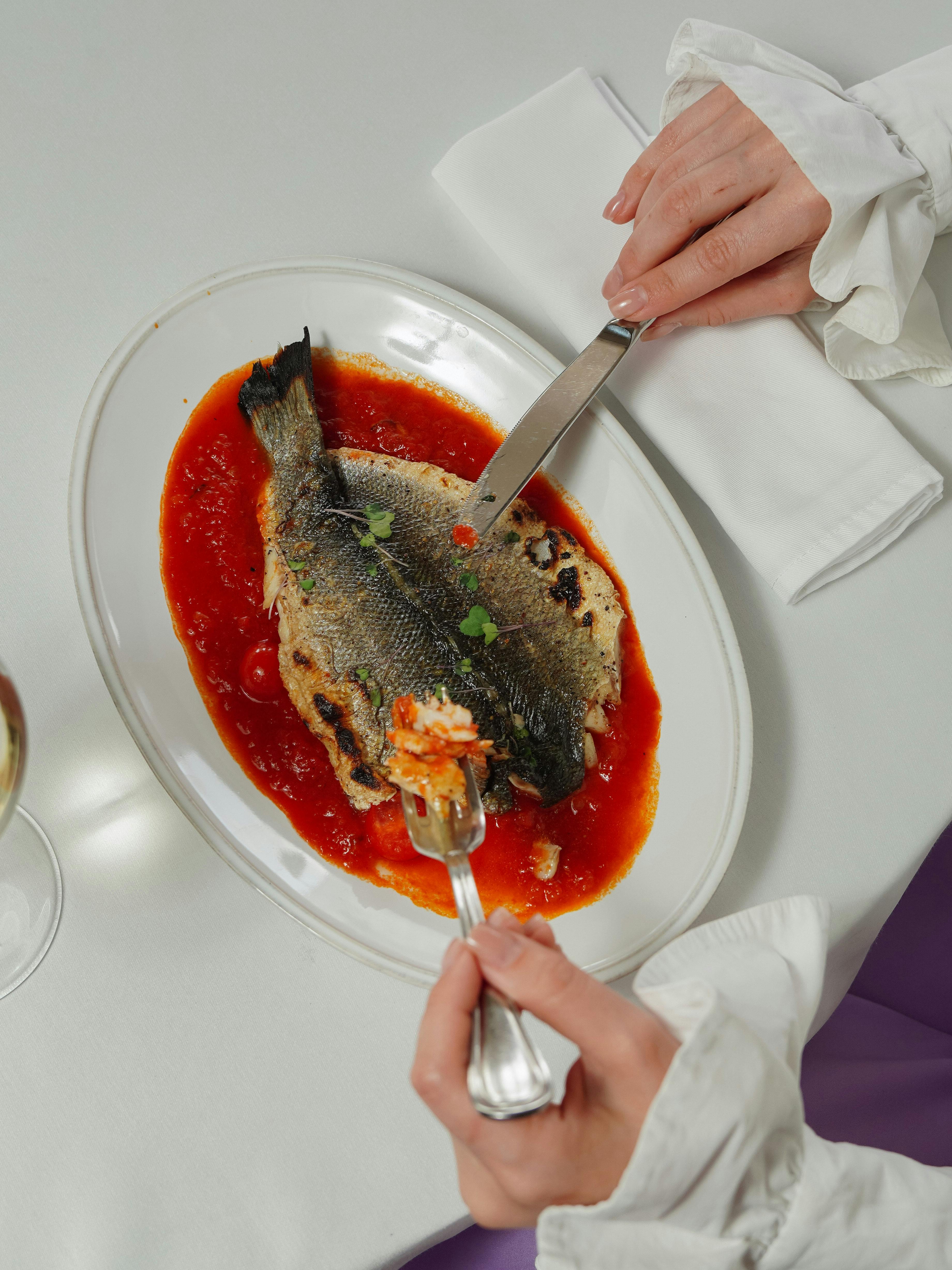 A person enjoying a whole cooked fish with tomato sauce, showcasing fine dining with elegance.
