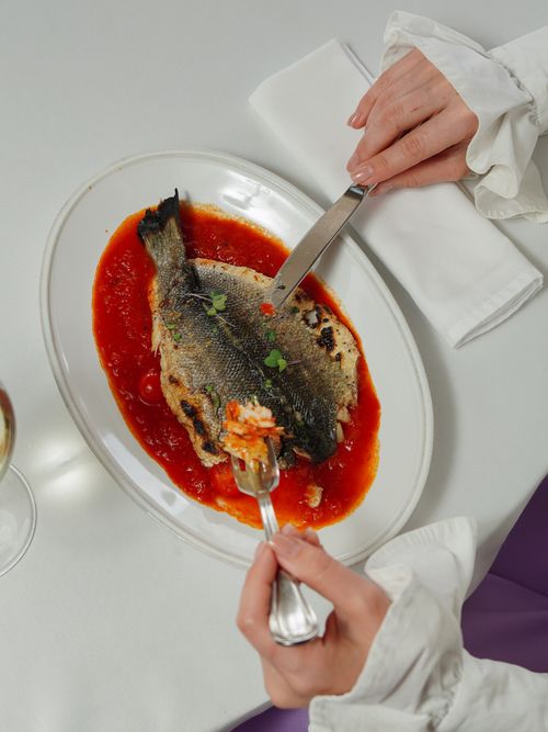 Free A person enjoying a whole cooked fish with tomato sauce, showcasing fine dining with elegance. Stock Photo