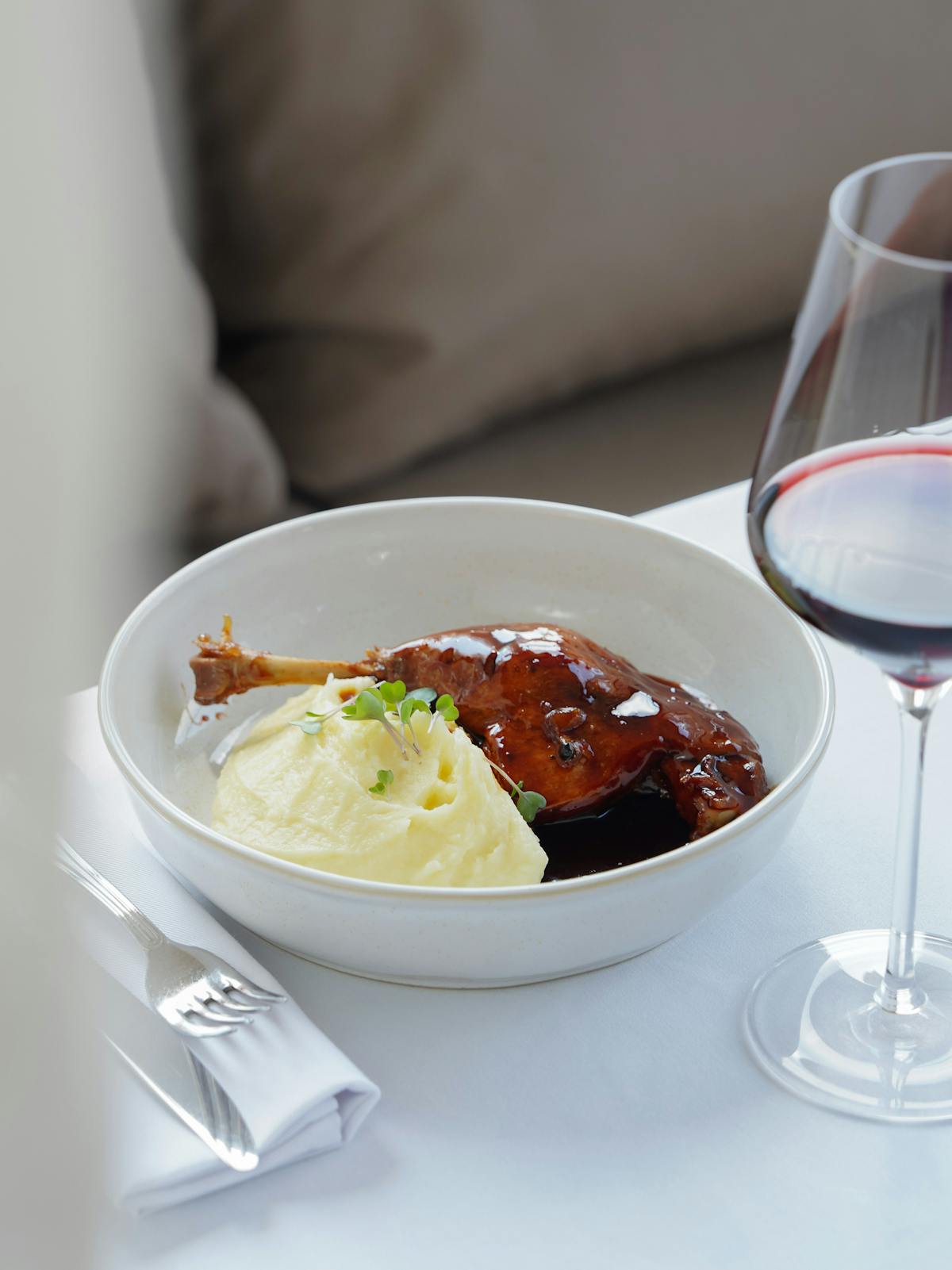 Piatto di anatra con purè e un calice di vino rosso sul tavolo