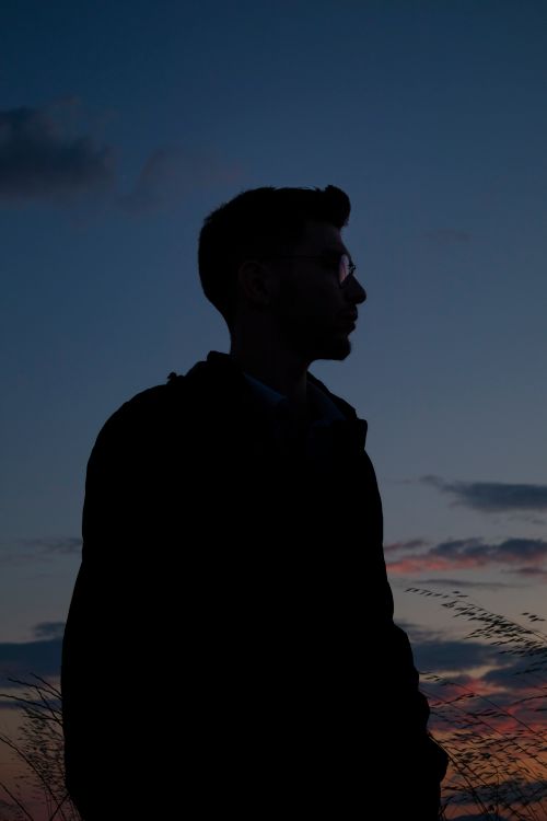 Free Silhouette of a man with eyeglasses standing outdoors at dusk, adding a moody and introspective vibe. Stock Photo