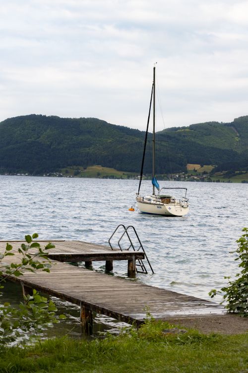 Free Tranquil scene of a sailboat near a wooden pier on Lake Attersee in Austria, surrounded by lush hills. Stock Photo