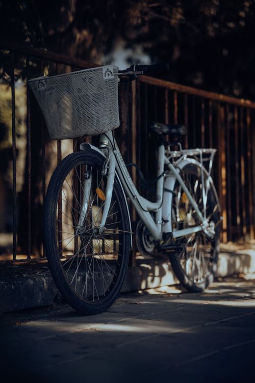 Free A white bicycle with a basket casts a shadow on the urban pavement near a railing. Stock Photo