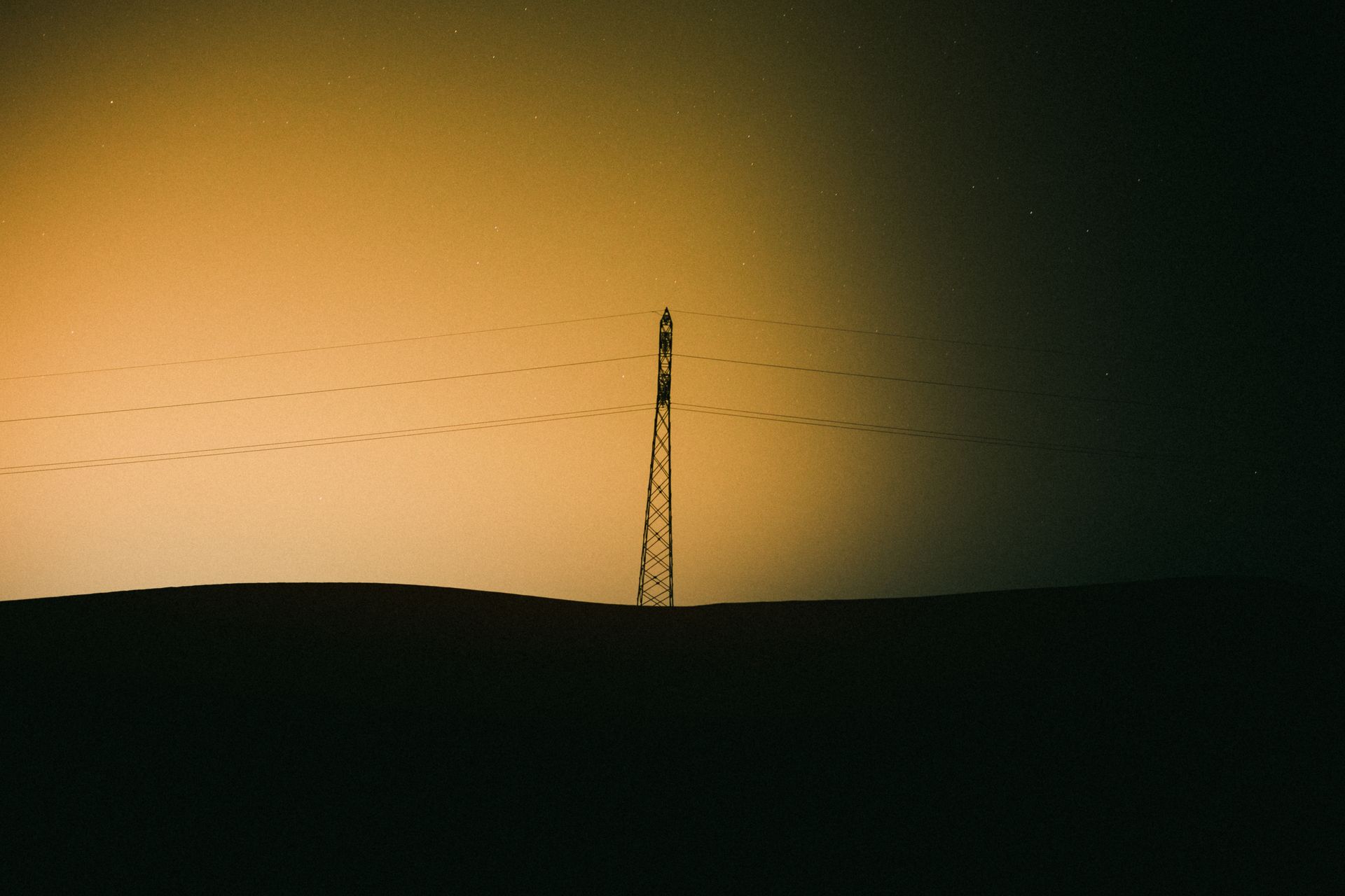 A transmission tower silhouetted against a vibrant sunset sky in Ouargla, Algeria.