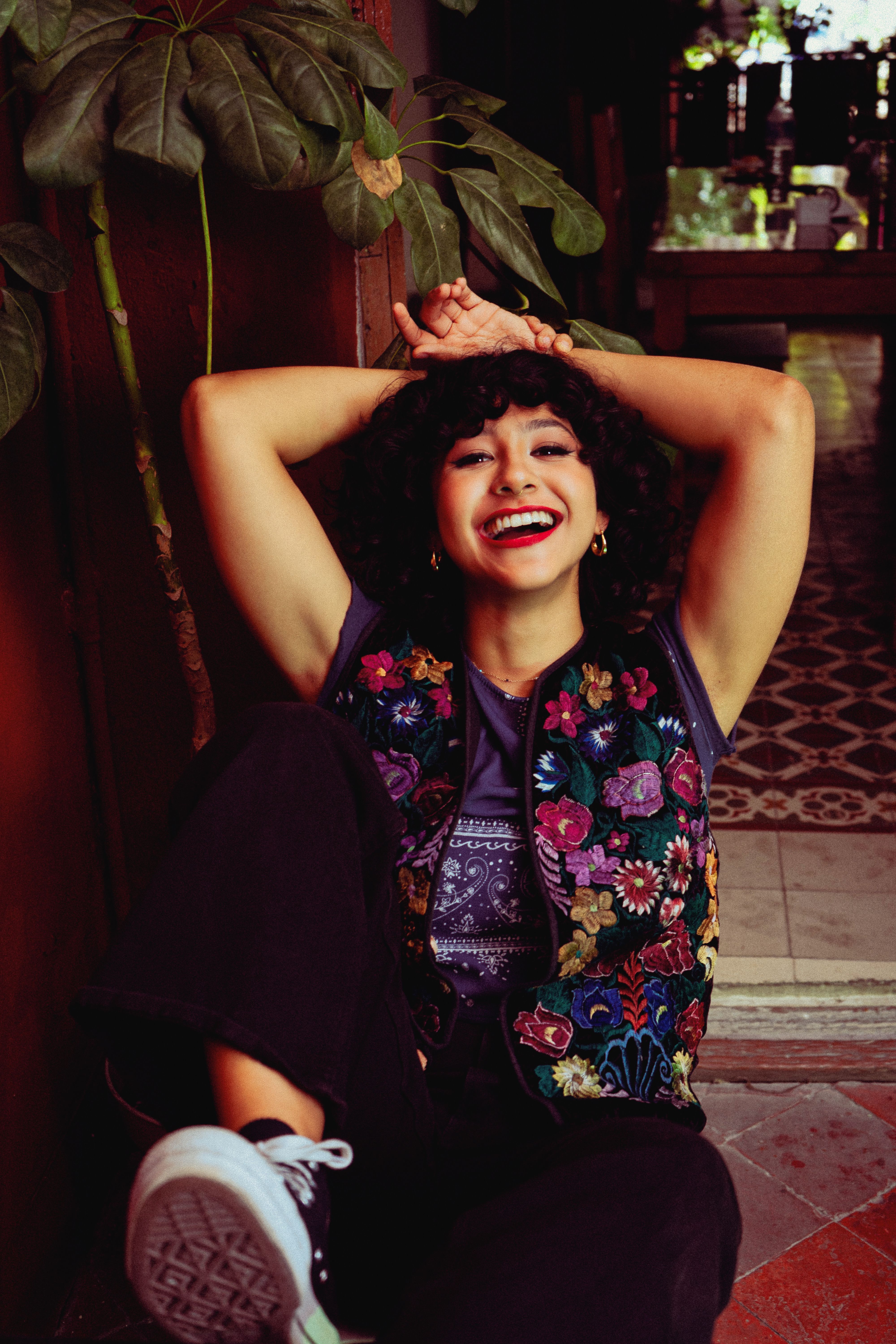 Joyful woman in floral blouse sitting indoors, exuding happiness and carefree vibes.