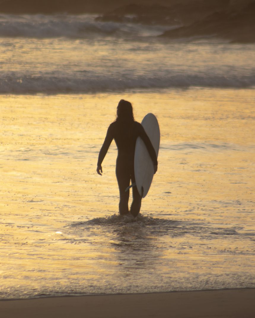 Surfer wading into golden evening water, photo by Carlos Reyes on Pexels