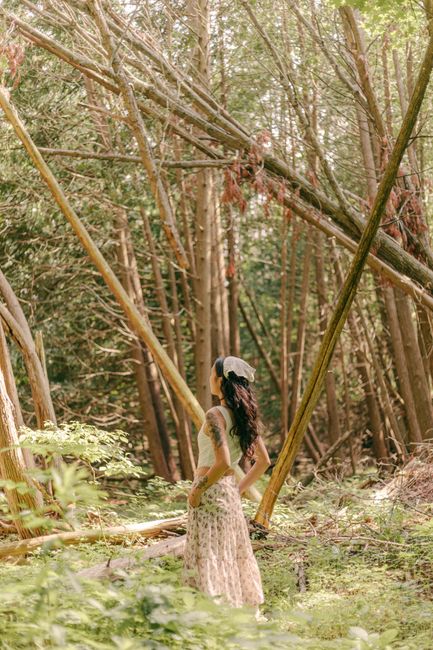 A young woman stands in a summer forest surrounded by fallen trees, embracing nature.