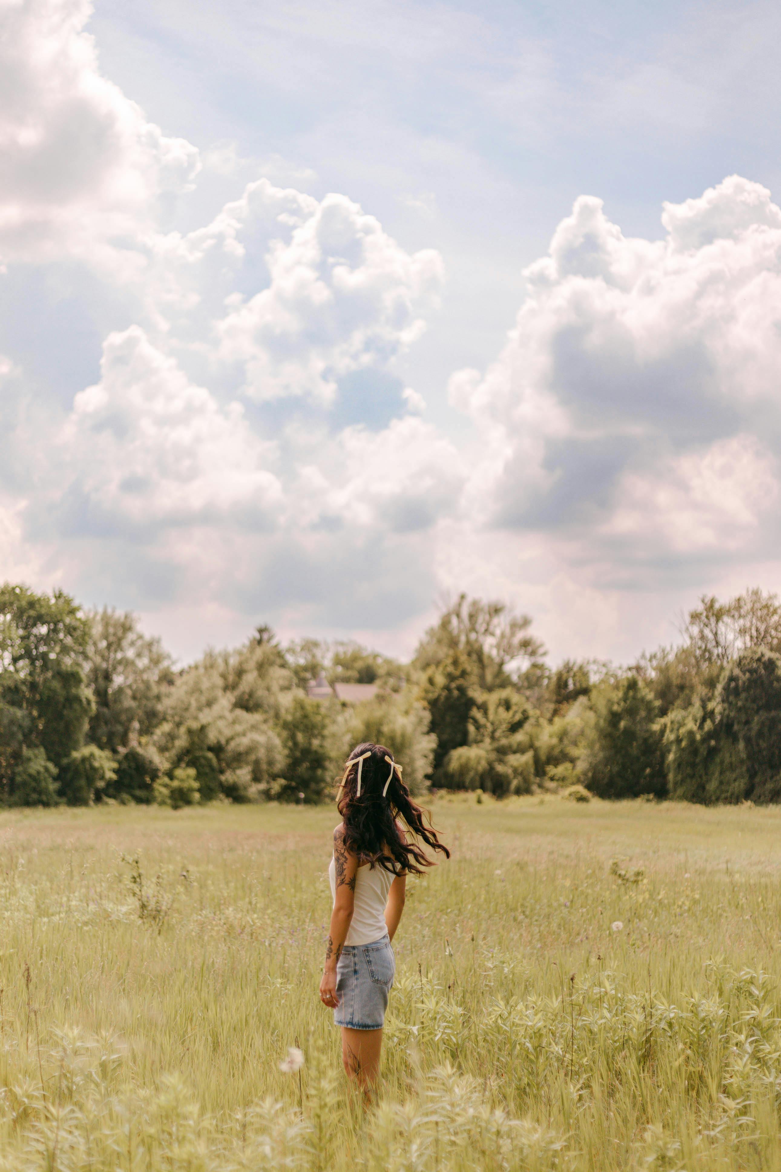 A woman enjoys a peaceful summer day in a lush field under a cloudy sky.
