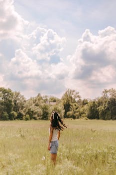 A woman enjoys a peaceful summer day in a lush field under a cloudy sky.