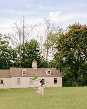 A young woman dances joyfully on a grassy lawn in front of a charming cottage during summer.