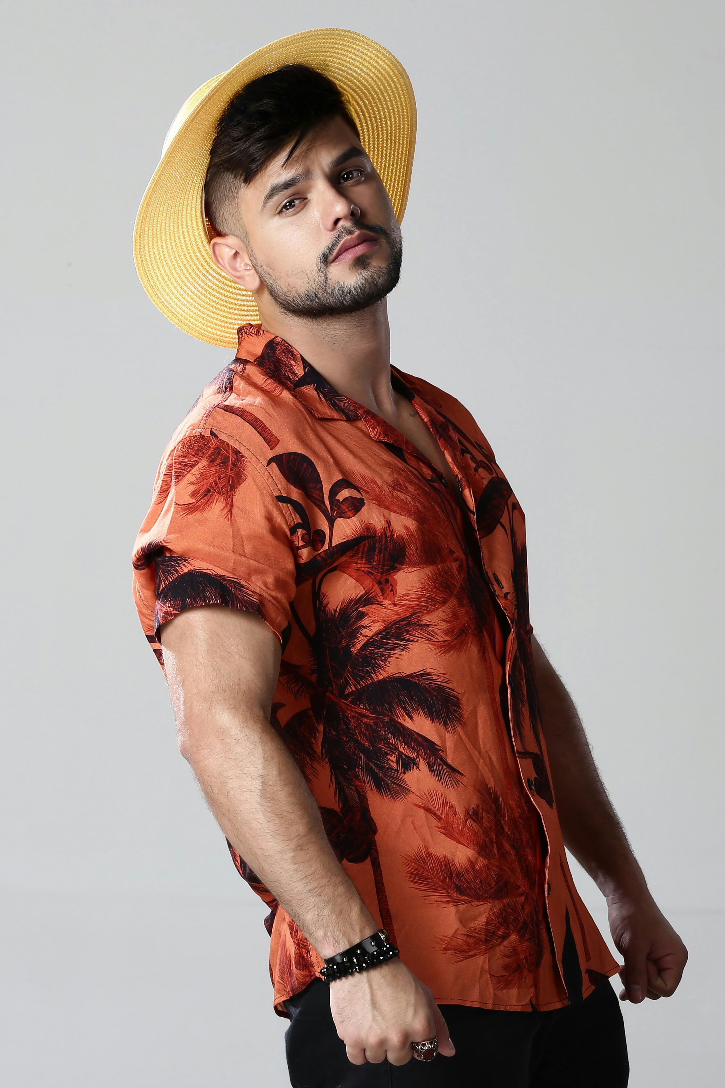Stylish young man in a Hawaiian shirt and yellow straw hat posing confidently in a studio setting.