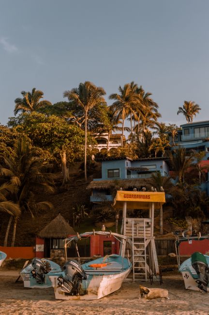 Idyllic Sayulita beach with boats and lifeguard hut against a tropical hillside at sunset.