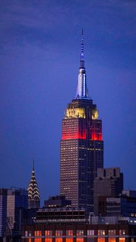 A vertical shot of the Empire State Building lit up at dusk, showcasing vibrant city life.