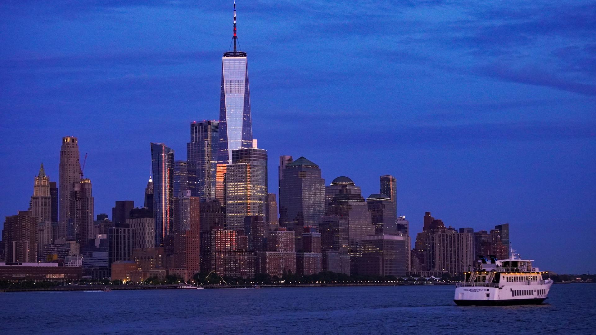 A stunning view of NYC skyline with ferry at twilight, featuring One World Trade Center.