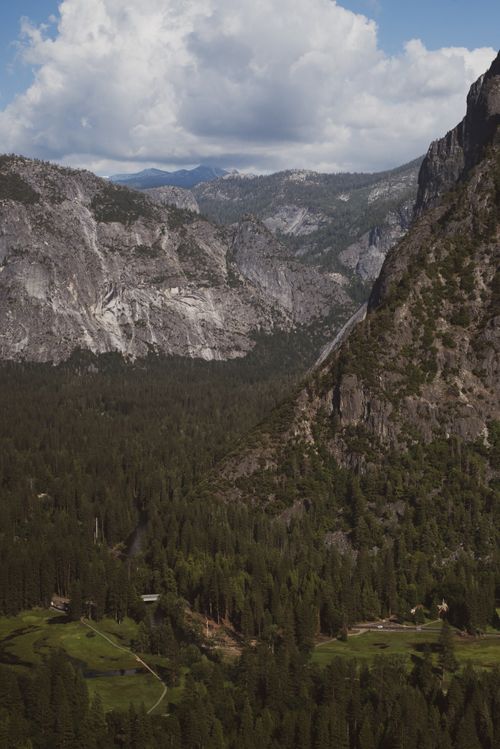 Free A breathtaking aerial view of a mountain valley with lush forests and rocky formations under a dramatic sky. Stock Photo