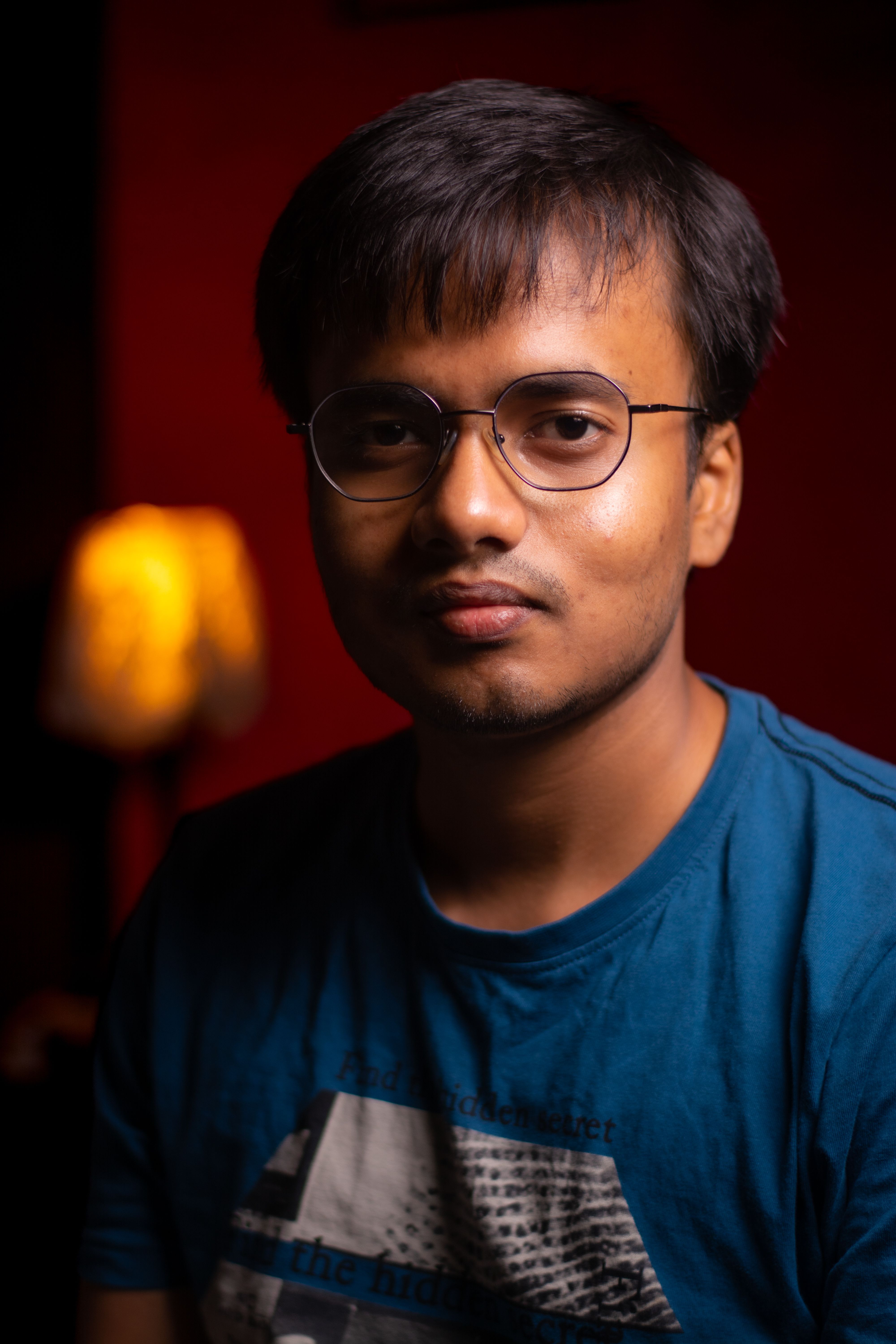 Casual portrait of a young man with glasses, captured indoors with warm lighting.