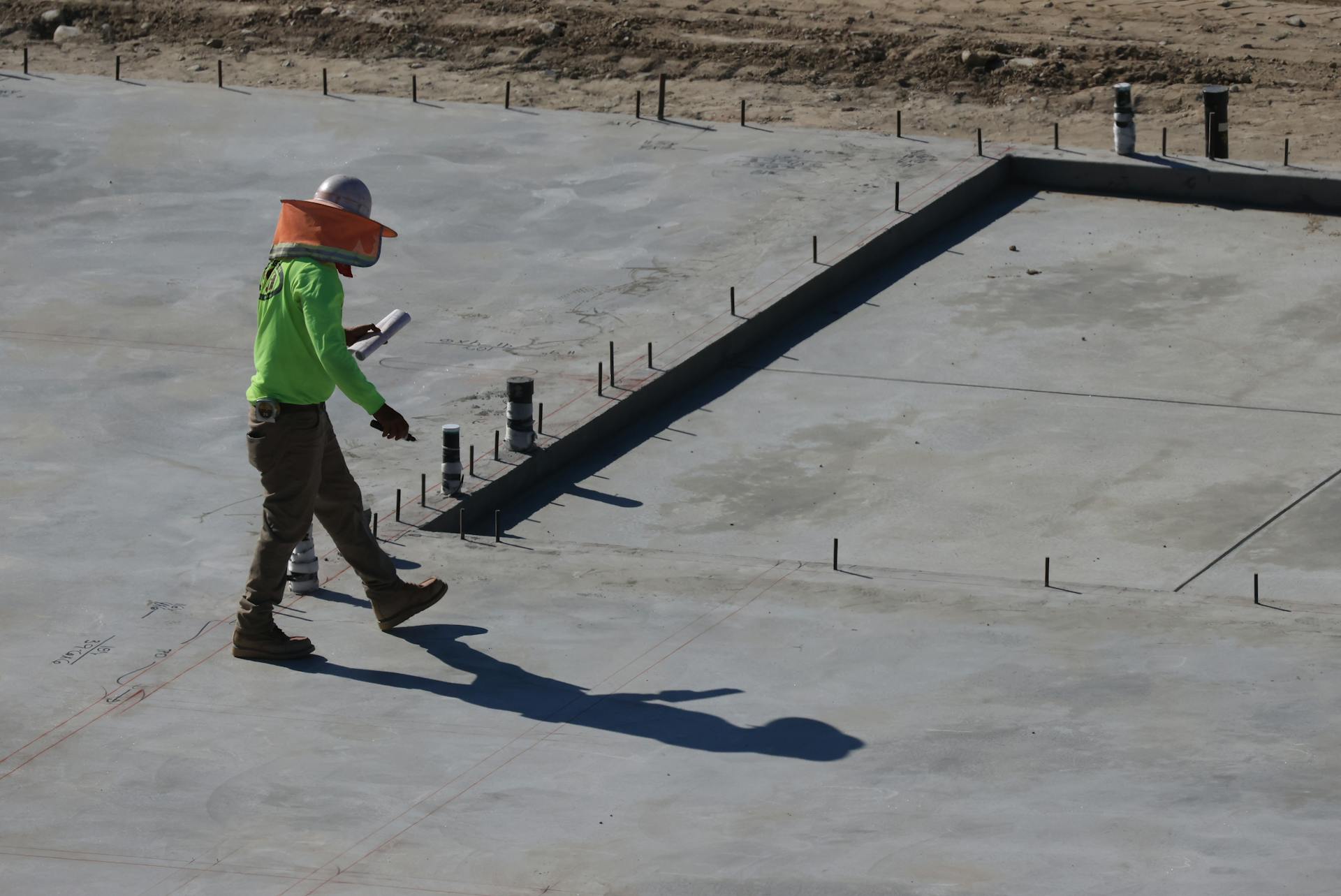 Engineer inspecting concrete slab at construction site in daylight.