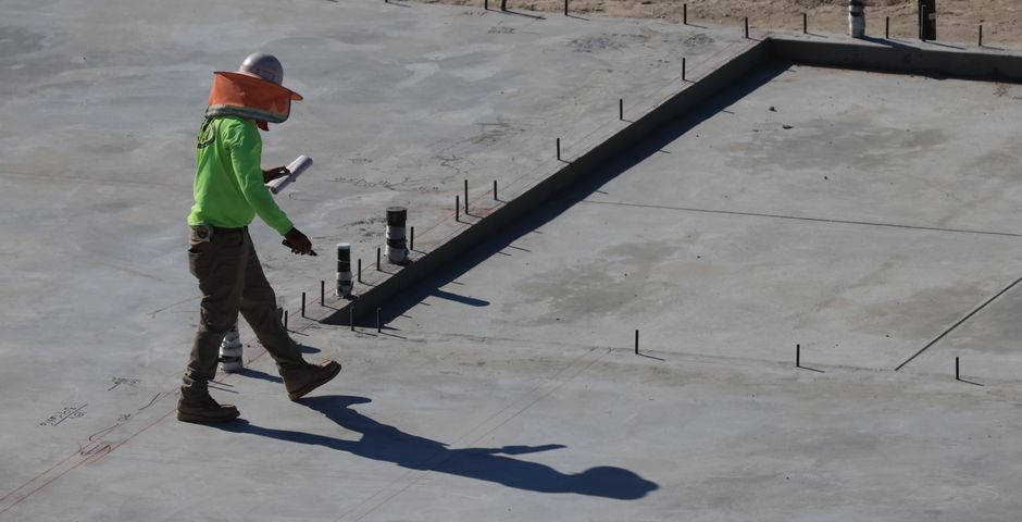 An engineer inspecting a concrete slab at a construction site — the barrier goes in before the slab is poured