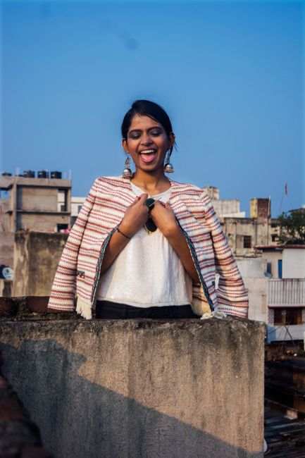 Laughing woman in striped cardigan enjoying a sunny day on a rooftop.
