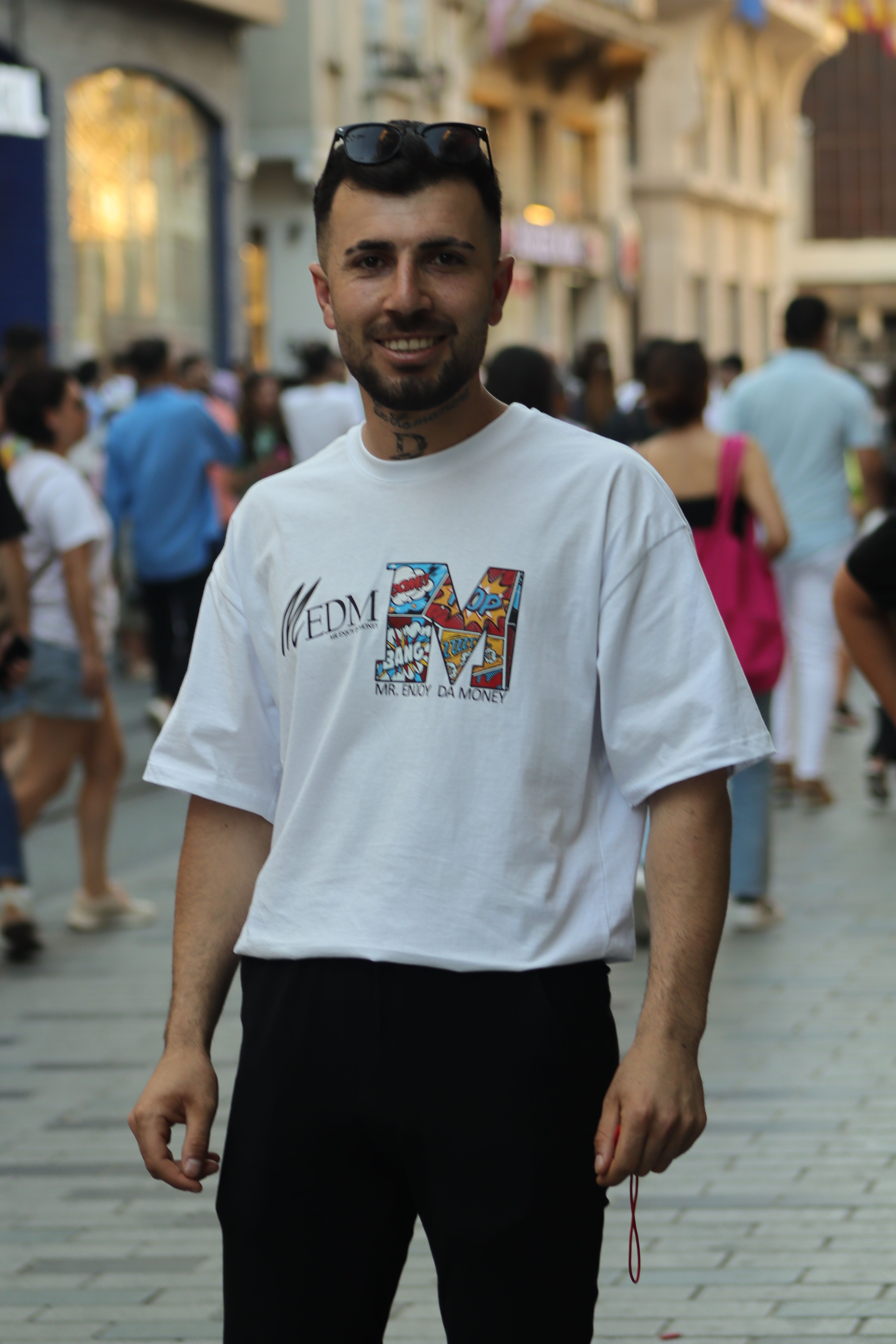 Man in casual white t-shirt and black pants smiling in a busy city street.