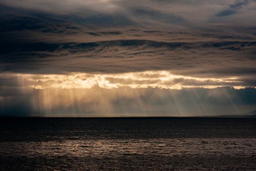 Free Scenic view of a dramatic overcast sky with sunbeams illuminating over the calm ocean, creating a mesmerizing and moody atmosphere. Stock Photo
