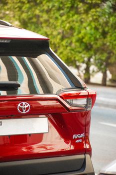 Rear view of a shiny red SUV parked on a city street with trees reflecting on the car's surface.