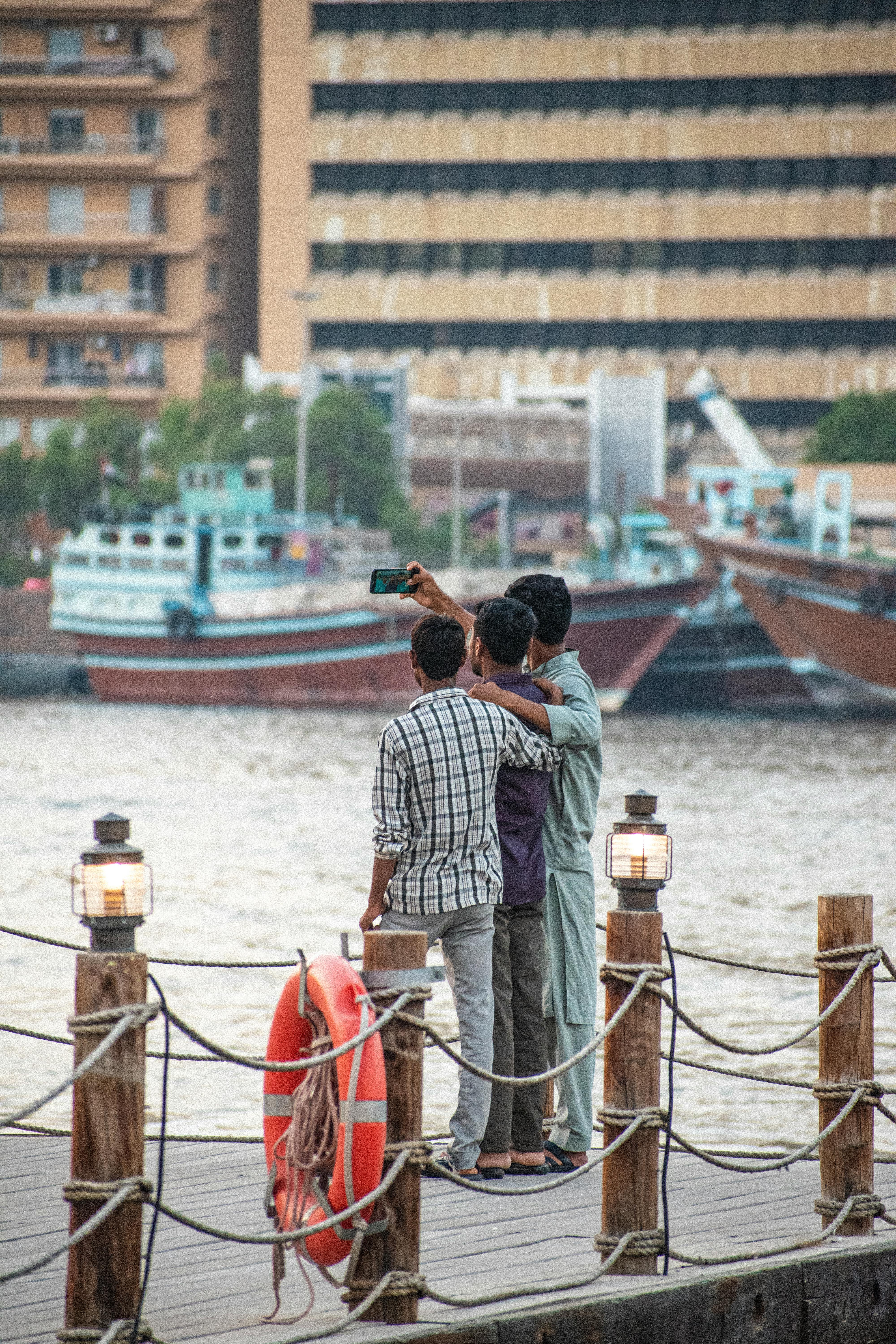 Free Three men take a selfie on a pier overlooking a busy river in an urban environment. Stock Photo